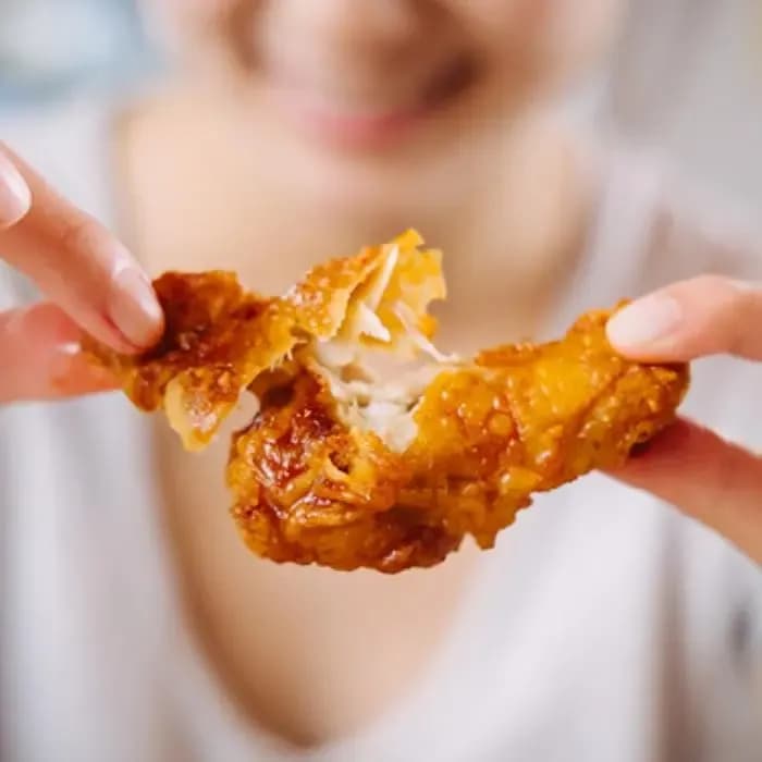 Person pulling apart a piece of Bonchon crispy fried chicken to show tender meat inside.
